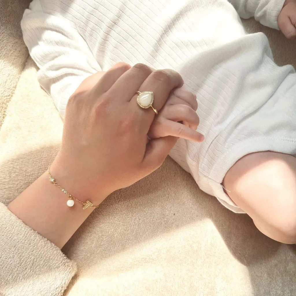 Main de maman avec bague de lait maternel qui tient main de bébé